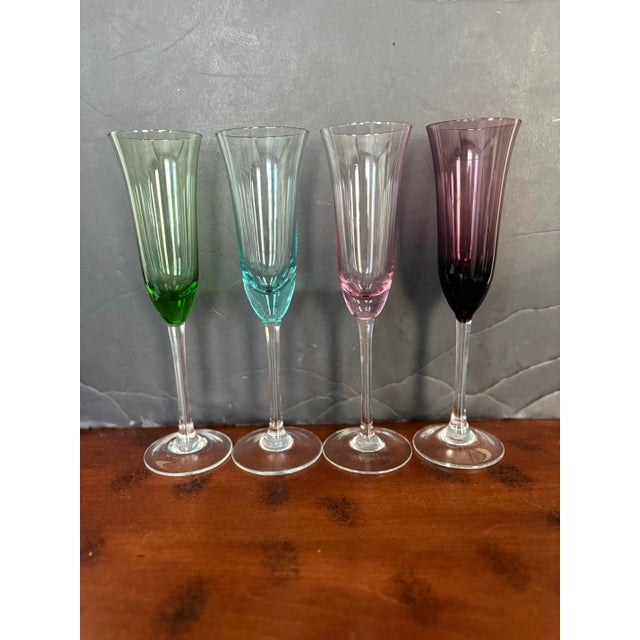 A beautiful set of four hand-blown art glass champagne flutes, featuring elegant clear stems and upper bowls with jewel-...