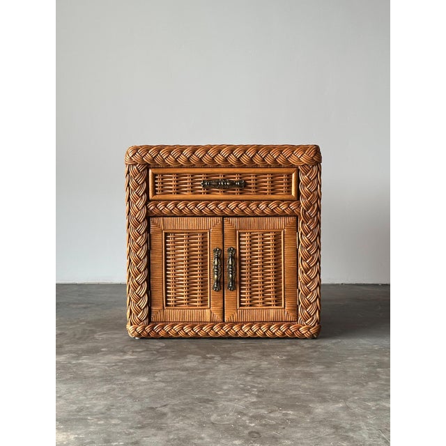 Fully wrapped in woven wicker, this vintage nightstand pairs a single drawer over a two-door cabinet, finished with hand-...