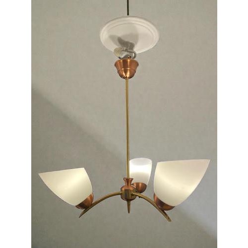 Swedish designer three-arm chandelier from the 1950s, executed in brass and copper with opaline glass shades. The fixture...