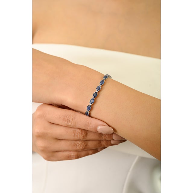 This luxurious tennis bracelet showcases oval-cut natural blue sapphires, each measuring approximately 6x4 mm and totaling...
