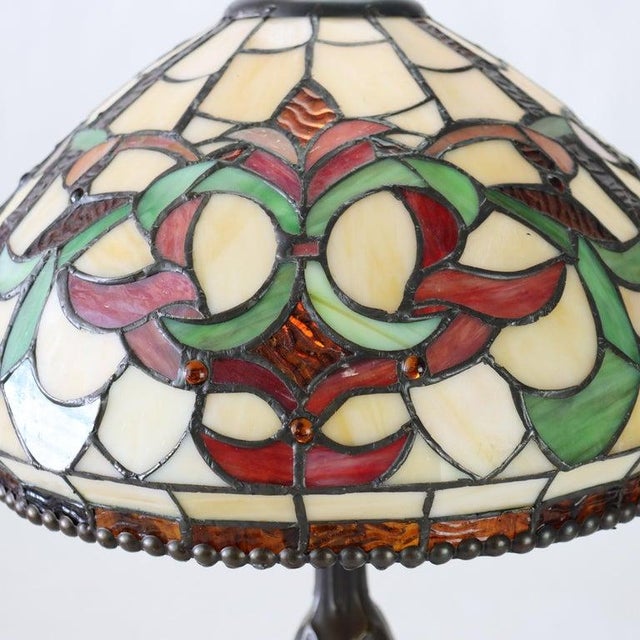 A vintage table lamp featuring a handcrafted leaded stained glass shade, characteristic of mid-20th century design. The...