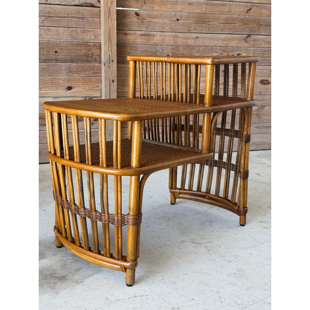 Charming and versatile vintage rattan tiered accent table featuring a warm honey-toned finish, woven rattan shelves, and...