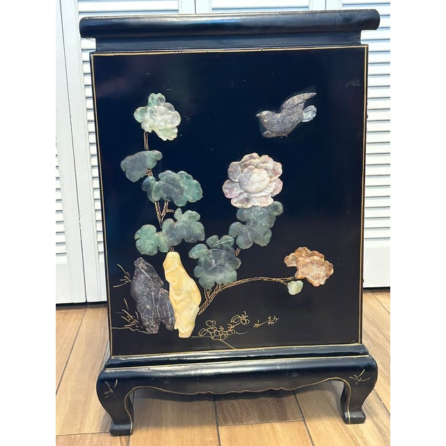A striking Chinese lacquered cabinet featuring an intricate composition of hardstone and soapstone inlay depicting...