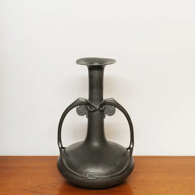 A Tudric pewter twin handled vase with a tall cylindrical neck and everted rim, the handles of sinuous organic form...