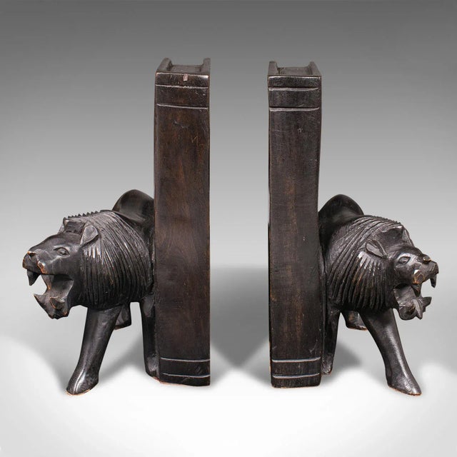 This is a pair of antique carved lion bookends. An Oriental, ebonised ironwood book rest with animal figure interest,...