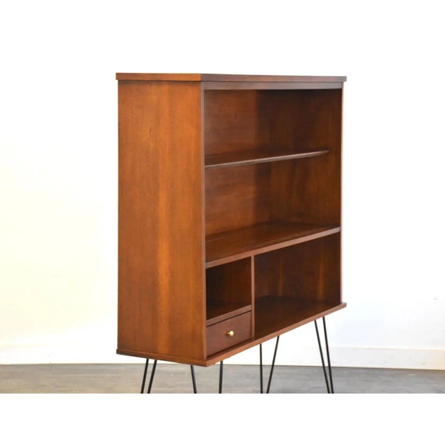 A mid century modern walnut bookcase with black hairpin legs and a chrome drawer pull. Professionally refinished. 46.75”...