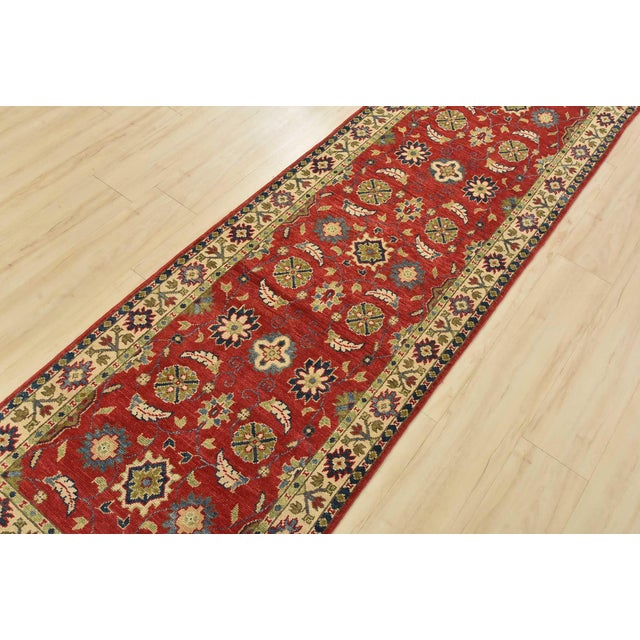 A traditional Kazak runner hand-knotted with fine wool on a cotton foundation. This oriental rug features a botanical...