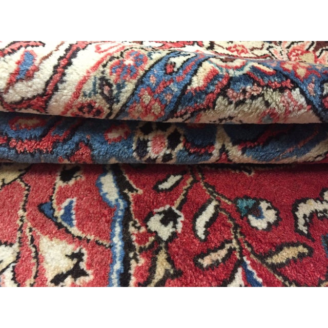 Vintage handwoven sarouk rug featuring an ornate design on a soft red field with light blue corner spandrels. Colors:...