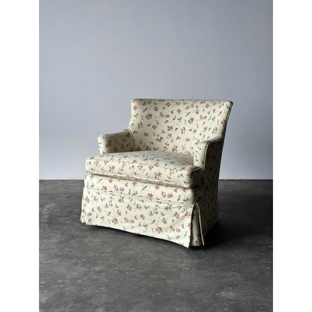 Cream chintz sprinkled with pink, mauve, and sage florals wraps this skirted vintage club chair from its curved back down...