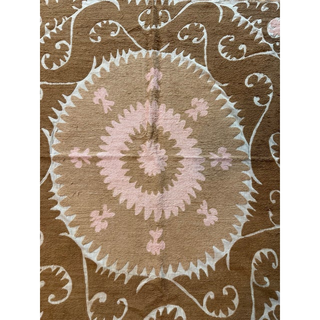Hand-embroidered Suzani panel from Uzbekistan — a tan starburst medallion with a pink rosette centre on an ivory ground,...