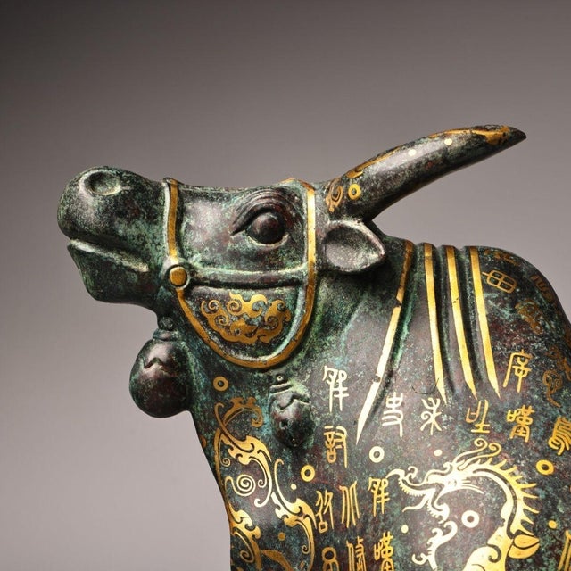The bull stands in a commanding pose with its head slightly raised. The surface is richly decorated with archaic-style...