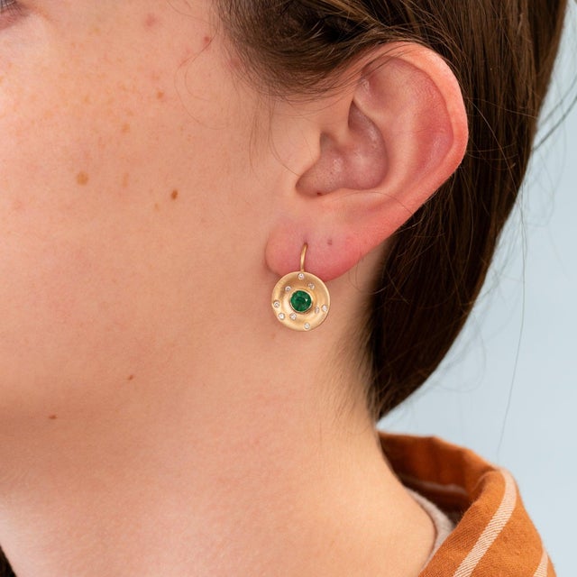 Vivid Zambian emeralds are set against brushed matte 14K yellow gold in these distinctive stud earrings, finished with...