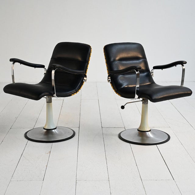 Set of two 1970s swivel armchairs with a steel frame and black vinyl upholstery with a contrasting back. A pair of swivel...