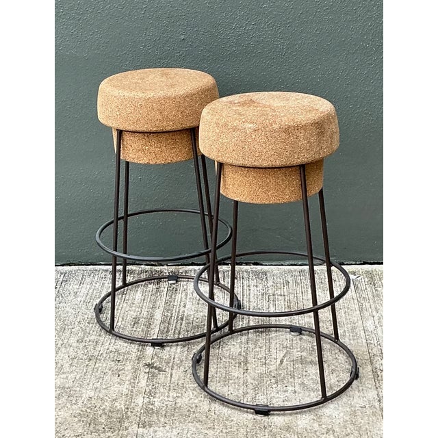 A pair of vintage bar stools featuring cork and metal construction, likely from the mid-20th century. The stools present a...