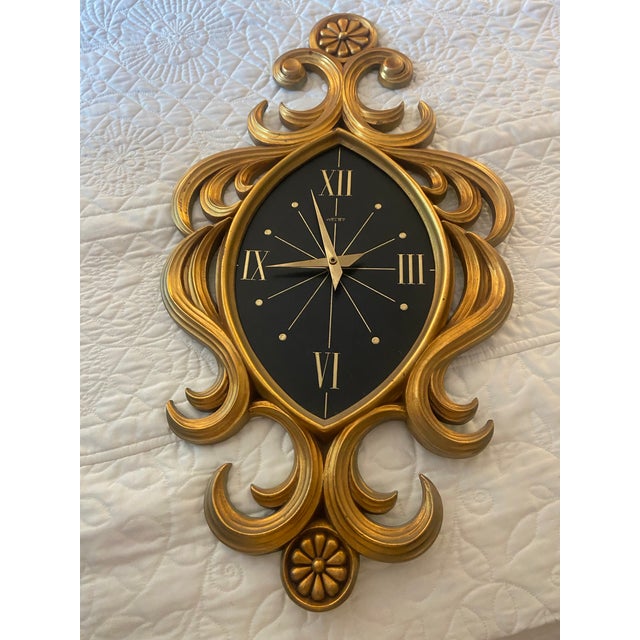 Striking vintage Welby wall clock featuring an ornate giltwood frame with sweeping scrollwork and floral rosette details....