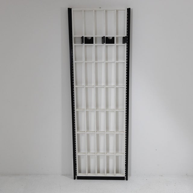 Wall-mounted coat rack with a white painted wooden grid structure, black painted wooden hooks, and a black painted metal...