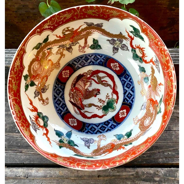 A striking Japanese Imari-style porcelain bowl featuring opposing dragons pursuing the sacred flaming pearl and a central...