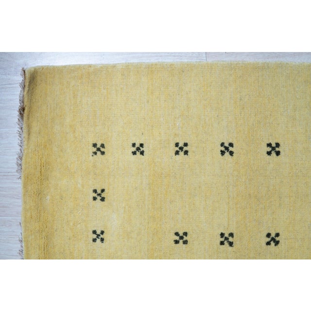 An 8' x 10' hand-knotted wool rug with a plain buttery yellow Gabbeh-style field with a simple dotted border in dark...