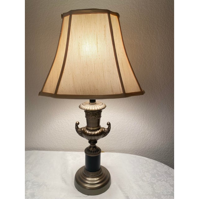 A neoclassical Hollywood Regency bronze trophy, cup earn style table, lamp, features and elegant, classical design with a...