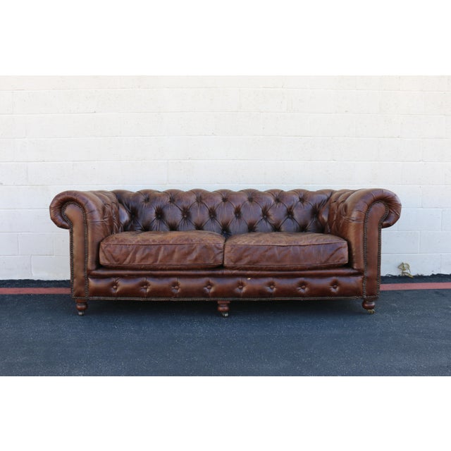 A timeless and inviting 21st-century English Chesterfield sofa by Restoration Hardware, beautifully crafted in rich brown...
