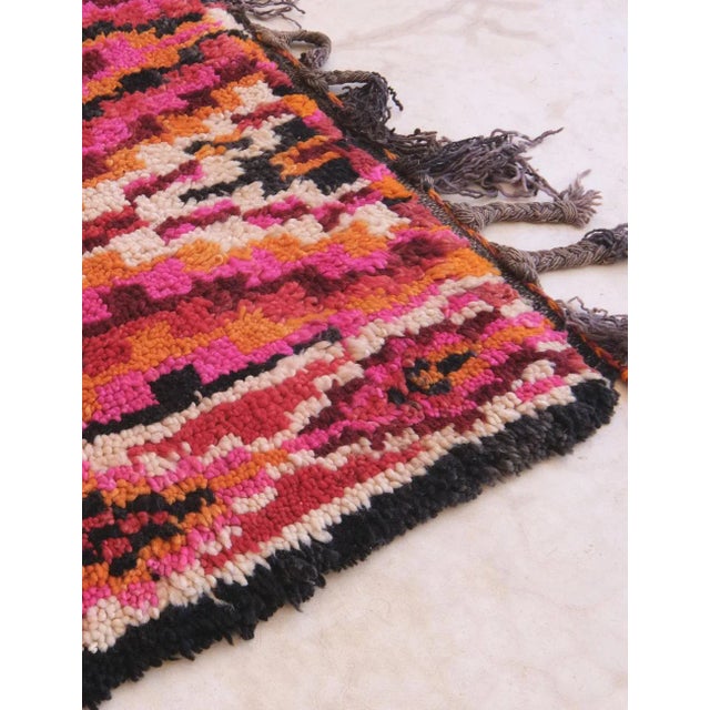 This vibrant tribal rug showcases a dynamic diamond lattice pattern filled with jagged, pixel-like details that evoke...