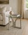 A distinctive vintage sculptural side table featuring a round clear-glass top supported by an architectural wooden tripod...