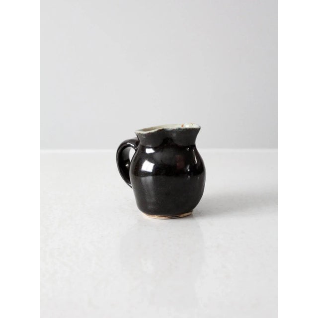 Vintage studio pottery creamer pitcher with a hand-thrown, artisan feel. This small ceramic pitcher features a deep black...