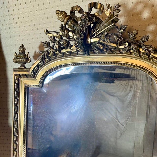 A large French wall or pier mirror with Neoclassical details, the arched top surmounted by a crest of crossed laurel...