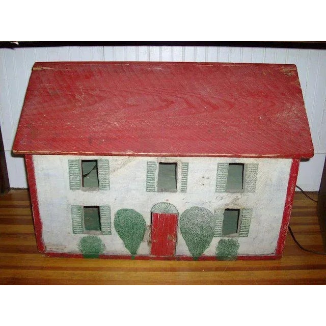 Antique paint decorated doll's house in shades of white, red and green with painted shutters and shrubs. Back is open and...