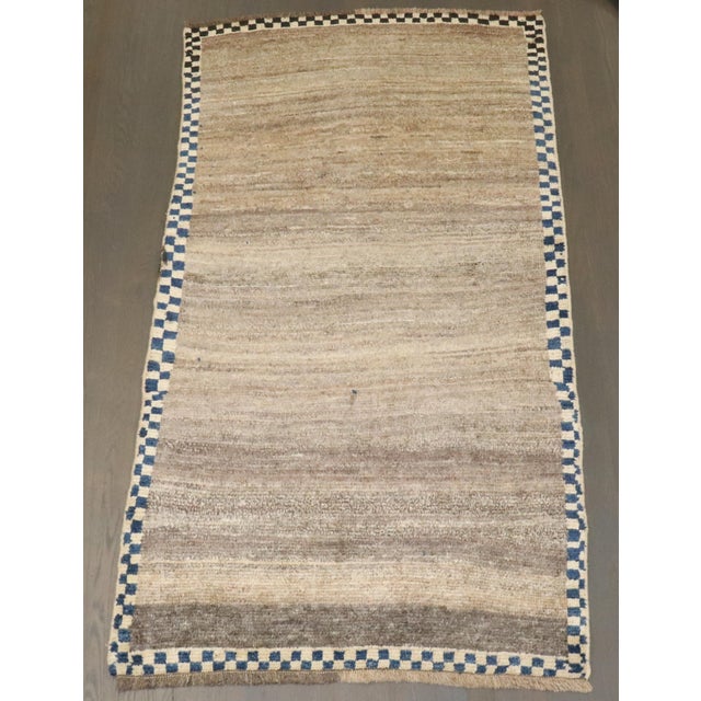 a 3rd quarter of the 20th Century Persian Gabbeh runner with a plain brown field surrounded by a narrow checkerboard...