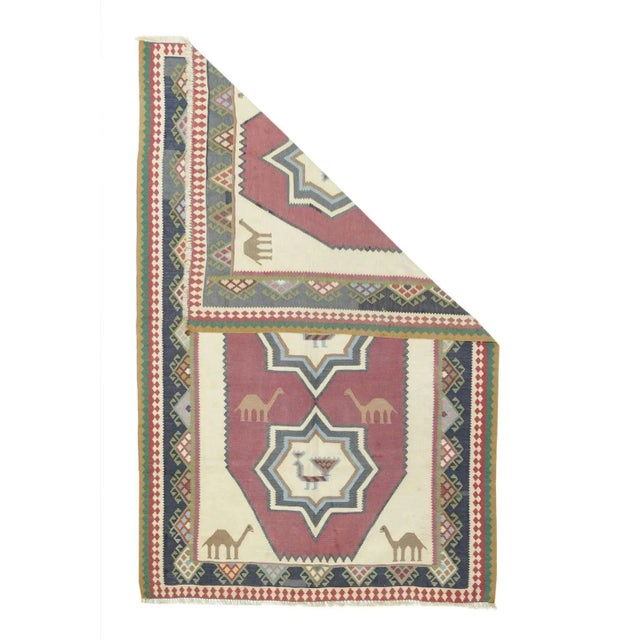 This vintage southwest Persian kilim shows a cream field with four corner dromedaries, enclosing as tall red octagonal...