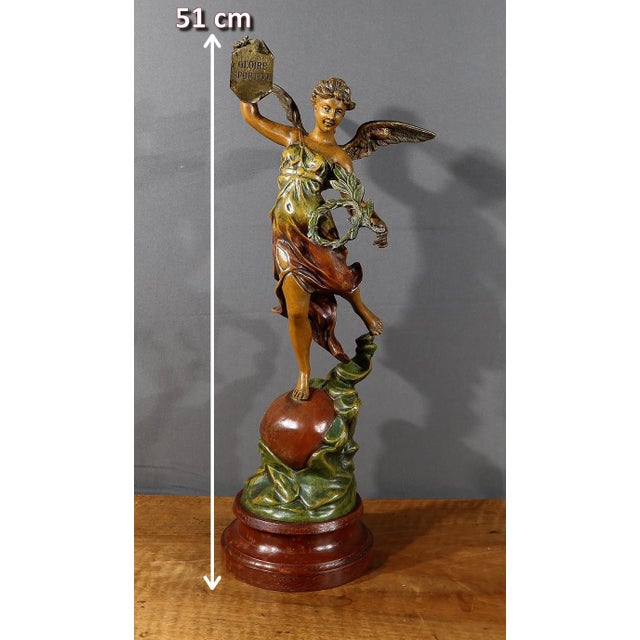 Large sculpture in patinated regula on a wooden base, featuring a winged young woman holding a leaf annotated "Gloire...