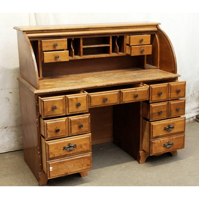 American Colonial style roll top desk in a medium wood tone. The desk pedestal features three drawers to either side and...