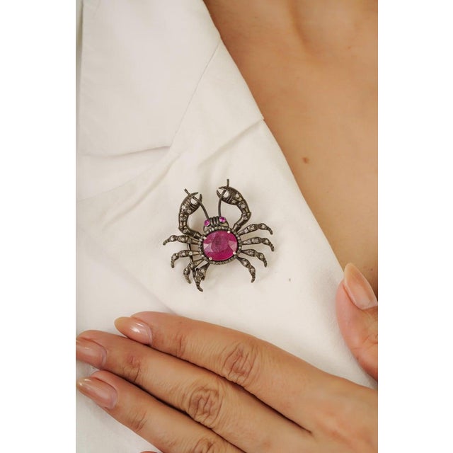 This whimsical ruby and diamond crab brooch is crafted in 925 sterling silver and showcases a vibrant 6.4 carat ruby...