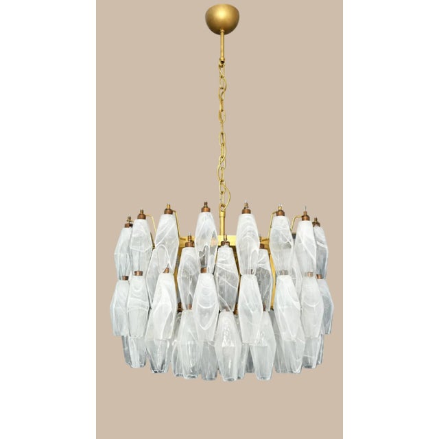 DUTIES FREE A sculptural chandelier featuring a circular metal structure with a refined gold finish, suspended from a...