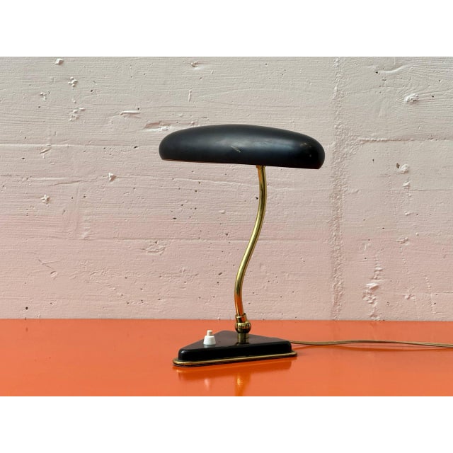 This elegant art deco table lamp captivates with its harmonious combination of a flat, oval-shaped metal shade in black...
