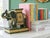 Vintage Hollywood Regency elephant bookends featuring richly detailed caparisoned elephants in deep green, gold, and ivory...