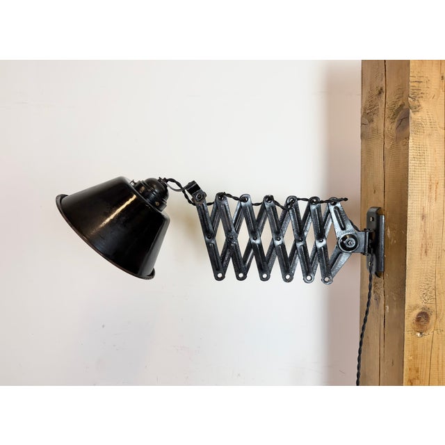This vintage Industrial adjustable scissor wall lamp was produced in Germany during the 1930s. The lamp has a black enamel...