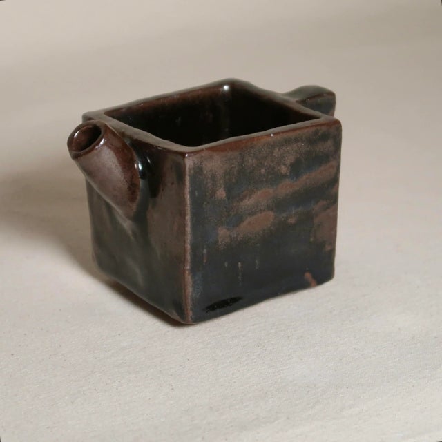This sculptural studio pottery vessel features a bold square form with an integrated handle and angled pour spout,...