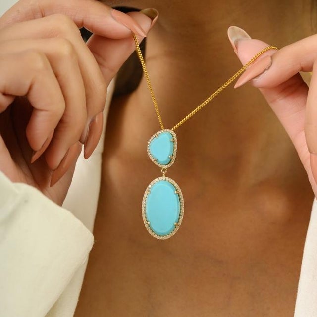 This striking double drop pendant showcases two vibrant natural turquoise cabochons totaling 12.2 carats. crafted in 14K...