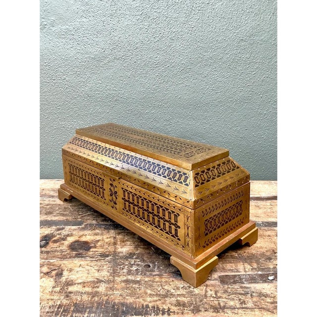 This vintage decorative box is entirely clad in brass over a wood core, its elongated rectangular form rising to a gently...