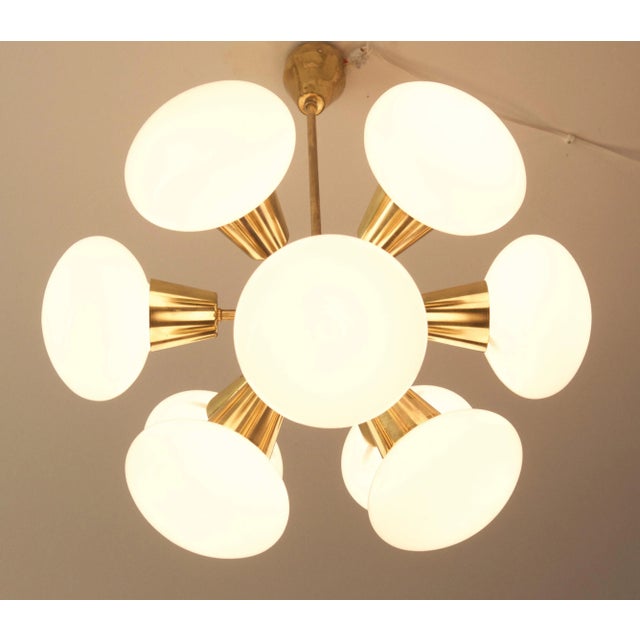 This space age chandelier originates from the 1960s. It is made from polished brass with nine round white opaline glass...
