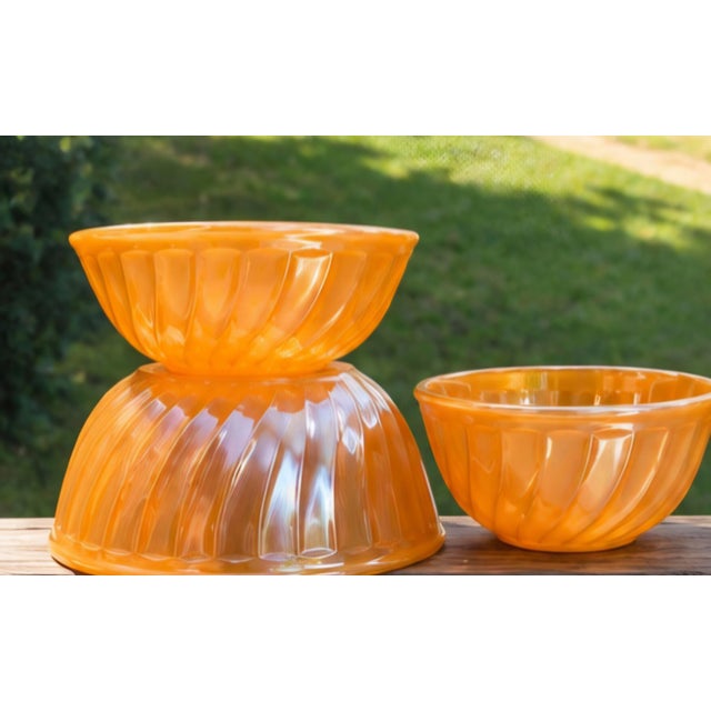 A striking set of three vintage Anchor Hocking Fire-King Peach Lustre Swirl nesting mixing bowls, dating to the mid-20th...