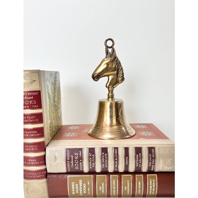 A vintage solid brass bell topped with a sculptural horse head finial, made in England and finished with a warm natural...