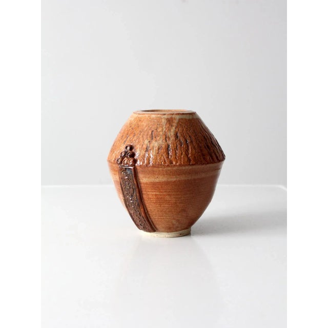 This is a vintage studio pottery vase. Signed by the artist, the art pottery features a decoratively carved front panel...