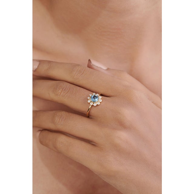 This sunburst halo ring featuring a vibrant 0.71 carat blue topaz and diamonds, set in 14K yellow gold. The center stone...