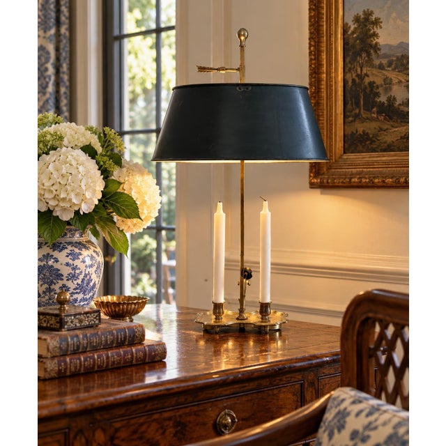 A classic bouillotte lamp rendered in warm brass, distinguished by its clean, tailored black tole shade. The form traces...