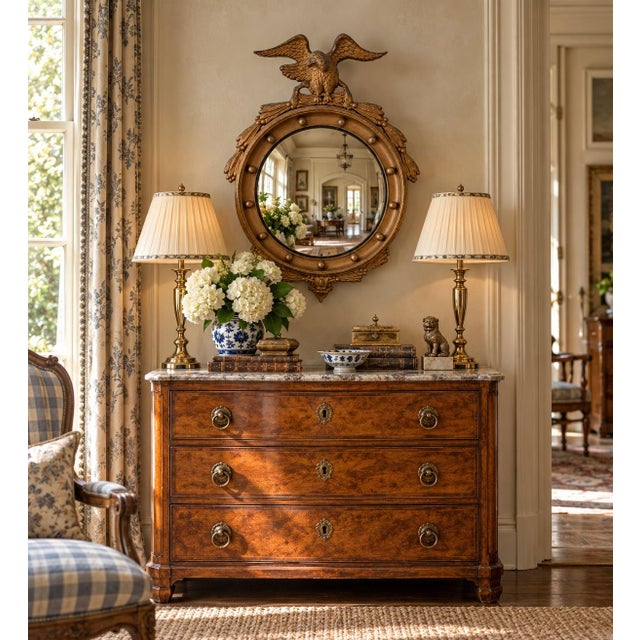 A Federal-style giltwood convex mirror crowned with a carved eagle, its wings outstretched above a laurel motif—an...