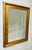 A striking contemporary wall mirror featuring a wide carved giltwood-style frame with warm antiqued gold finish and clean...