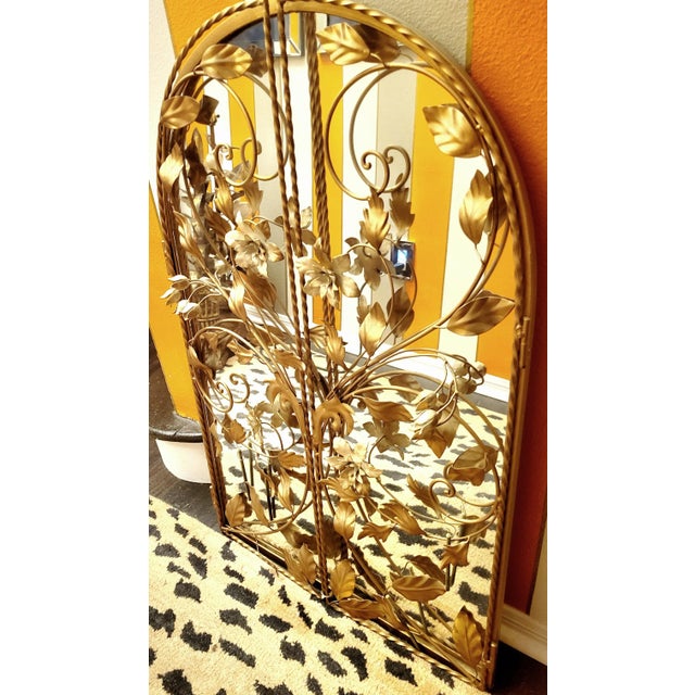 A beautiful vintage gold tole floral arched wall mirror. The mirror features pretty metal tole flowers with braided trim....